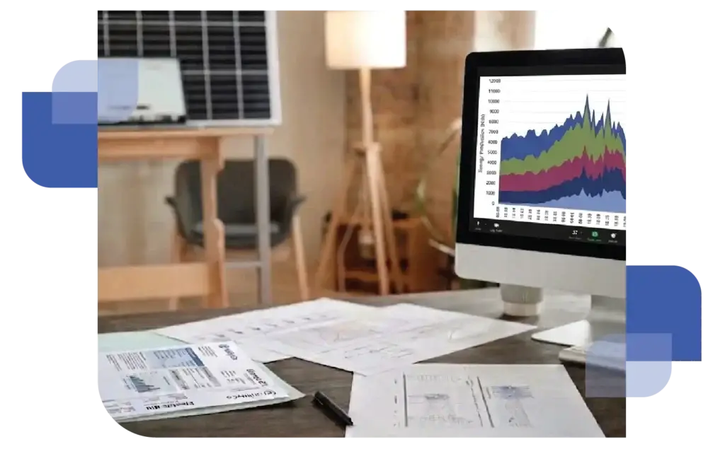 A professional workspace featuring a solar panel setup, a desk lamp, and a desktop computer screen displaying various energy data charts and graphs, representing sustainable energy management.